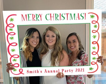 May include: Three women pose for a photo with a red and green Christmas-themed photo booth prop. The prop has the words "Merry Christmas!" and "Smith's Annual Party 2021" printed on it.