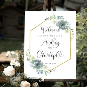 May include: Welcome to our wedding sign with a gold hexagonal frame and watercolor greenery. The sign reads "Welcome to our wedding Audrey and Christopher May 24, 2019".