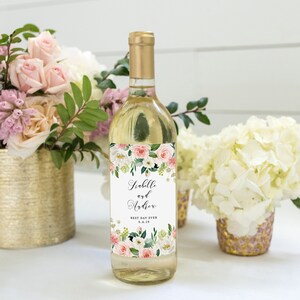 May include: A white wine bottle with a floral wedding label. The label features pink and white flowers with green leaves and the text "Isabelle and Arthur Best Day Ever 5.4.18".