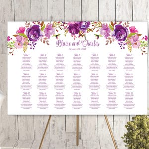 May include: A wedding seating chart sign featuring a white background with a floral arrangement of purple and pink watercolor roses at the top. The text reads Blaire and Charles, October 20, 2018, followed by a list of 21 tables with names.
