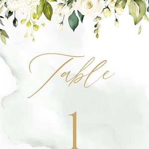 May include: White floral wedding table number card with green leaves and a gold background. The card says "Table 1".
