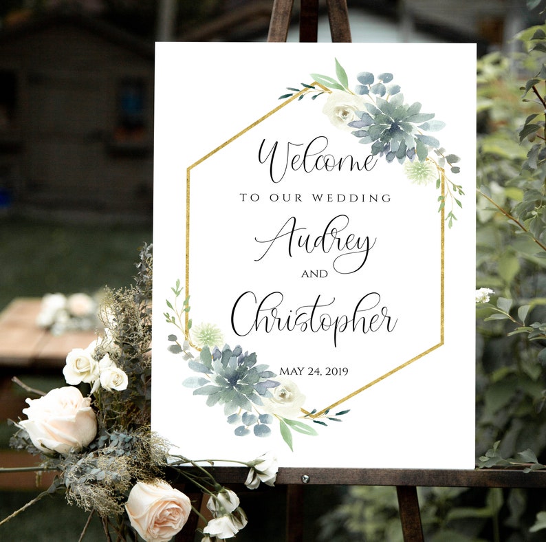 May include: Wedding welcome sign with a gold geometric frame and watercolor greenery. The sign reads "Welcome to our wedding Audrey and Christopher May 24, 2019".