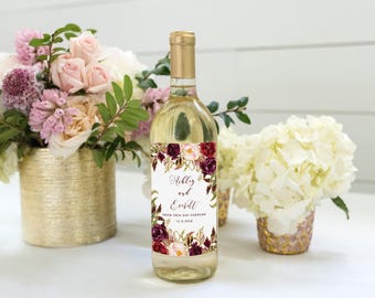 Könnte beinhalten: Eine Weinflasche aus Klarglas mit einem weißen rechteckigen Etikett, das einen floralen Rand aus dunkelburgunderfarbenen und zartrosa Blüten aufweist. Der Text lautet Ashley and Everitt FROM THIS DAY FORWARD 11.3.2019 in Schrift.