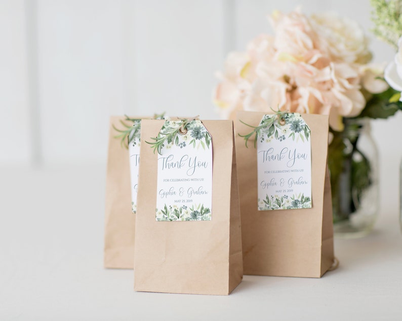 May include: Three brown paper bags with thank you tags attached. The tags are white with green floral designs and the text "Thank You for celebrating with us Sophia & Graham May 23, 2019".