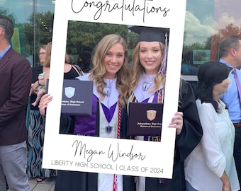 May include: A white rectangular graduation photo frame prop featuring a black mortarboard icon, the text Congratulations, the name Megan Windsor, and the text LIBERTY HIGH SCHOOL | CLASS OF 2024 in black lettering on a white background.