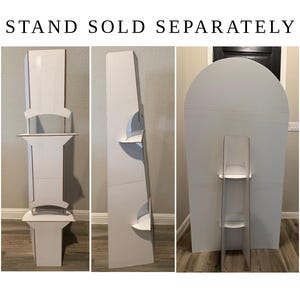 May include: A white cardboard display stand with multiple shelves, shown from three different angles. The text STAND SOLD SEPARATELY is printed at the top. The structure features a tall vertical back panel and several horizontal shelves.