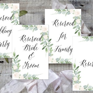 K&ouml;nnte beinhalten: Vier wei&szlig;e Karten mit gr&uuml;nen floralen R&auml;ndern und schwarzem Kalligraphietext. Der Text lautet "Reserviert Hochzeitsfeier", "Reserviert Braut & Br&auml;utigam", "Reserviert f&uuml;r die Familie" und "Reserviert".