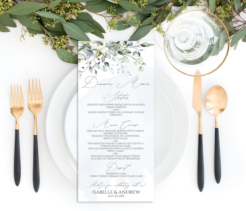May include: A wedding menu card with a watercolor design of eucalyptus leaves and white flowers. The menu includes appetizers, main course, dessert, and a thank you note for Isabelle & Andrew, July 20, 2019.