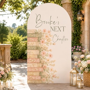 May include: An arched white event sign featuring the text Brooke's NEXT Chapter in gray script and block lettering. The left side displays a vertical stack of illustrated books in muted pink and green tones, accented with soft pink floral vines.