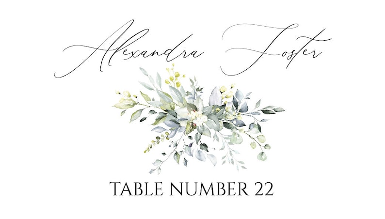 May include: A white card with a floral design in shades of green and white. The text "Alexandra Foster" is written in cursive at the top of the card. The text "TABLE NUMBER 22" is written in black at the bottom of the card.