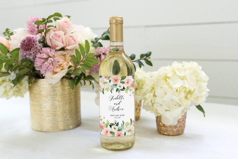 May include: A white wine bottle with a floral wedding label. The label features pink and white flowers with green leaves and the text "Isabelle and Arthur Best Day Ever 5.4.18".