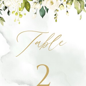 May include: White floral wedding table number card with gold calligraphy that says "Table 2" on a light green watercolor background.