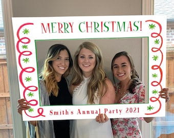 May include: A rectangular white photo booth frame featuring a red and green border with swirling lines and star accents. The top text reads MERRY CHRISTMAS! in red and green, while the bottom text reads Smith's Annual Party 2021 in red.
