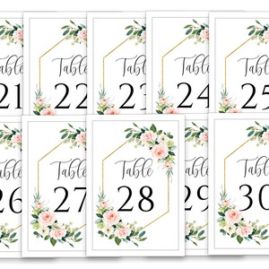 Puede incluir: Diez tarjetas de n&uacute;mero de mesa blancas con marcos geom&eacute;tricos dorados y dise&ntilde;os florales. Los n&uacute;meros van del 21 al 30.