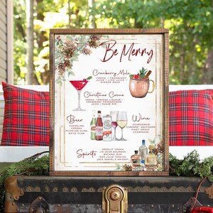 May include: A rectangular wooden-framed sign with the text Be Merry, featuring watercolor illustrations of cocktails, beer, and wine. It lists ingredients for a Cranberry Mule and Christmas Cosmo, alongside various beer and spirit labels.
