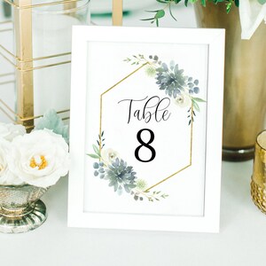 May include: White table number card with a gold hexagonal frame and blue and white floral design. The card says "Table 8" in black text.