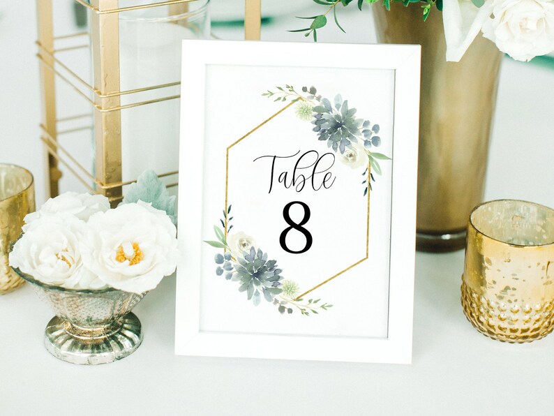 May include: White table number card with a gold hexagonal frame and blue and white floral design. The card says "Table 8" in black text.