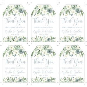 May include: Six white wedding favor tags with a watercolor design of green leaves and blue flowers. The text on the tags reads "Thank You" with the names "Gophia & Graham" and the date "May 25, 2019".
