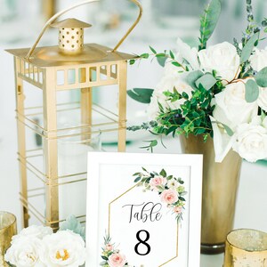 Puede incluir: Tarjeta de n&uacute;mero de mesa blanca con un marco hexagonal dorado y un dise&ntilde;o floral rosa. La tarjeta dice "Mesa 8".