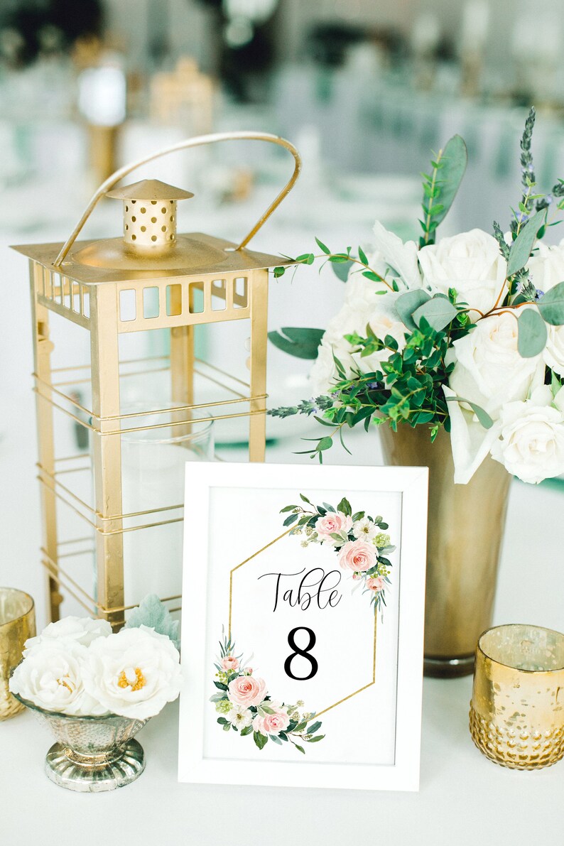 Puede incluir: Tarjeta de n&uacute;mero de mesa blanca con un marco hexagonal dorado y un dise&ntilde;o floral rosa. La tarjeta dice "Mesa 8".