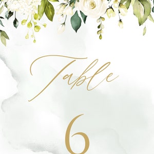 May include: White floral wedding table number card with green leaves and a gold background. The card says "Table 6".