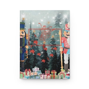 May include: A journal with a watercolor illustration of a ballerina, Christmas trees, and nutcrackers. The cover features a winter scene with a ballerina in a red outline, surrounded by Christmas trees, poinsettias, and gifts.