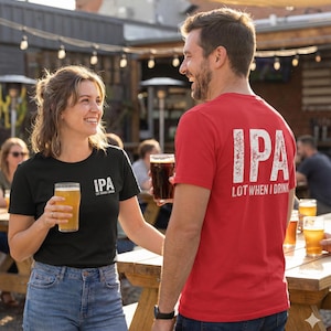 Può includere: Una donna e un uomo sorridono e tengono bicchieri di birra. La donna indossa una maglietta nera con la scritta "IPA LOT WHEN I DRINK". L'uomo indossa una maglietta rossa con lo stesso testo sul retro. La scena si svolge all'aperto.