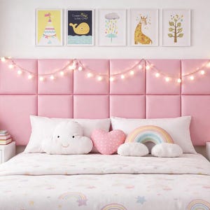 May include: A pink bedroom with a bed featuring a pink headboard, white bedding, and decorative pillows. The room is decorated with framed art, a string of lights, and a bunny-shaped lamp. The overall theme is a child's bedroom.