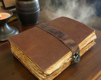 Può includere: Un diario rilegato in pelle marrone con chiusura a cinturino. Le pagine hanno un aspetto vintage e invecchiato. Il diario è su una superficie di legno, con una candela accesa e un contenitore scuro sullo sfondo.