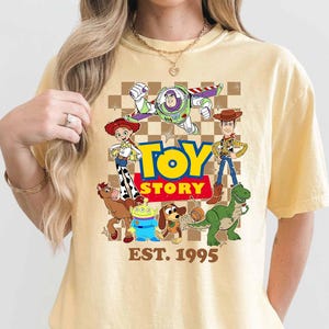 A person wearing a yellow t-shirt with a graphic design featuring characters from the Toy Story movie franchise.