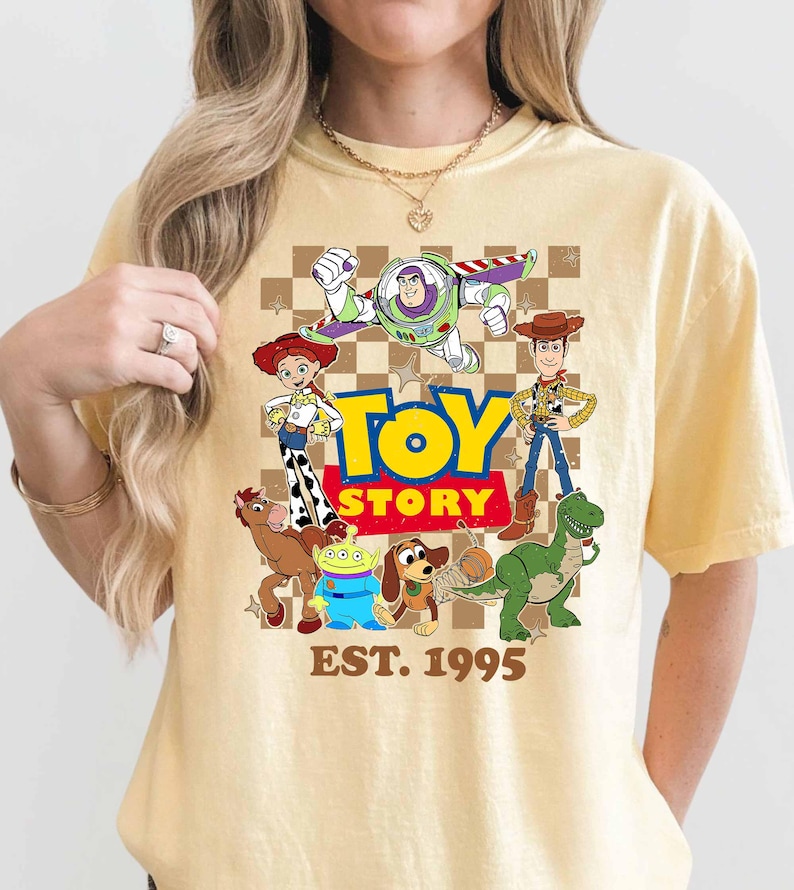 A person wearing a yellow t-shirt with a graphic design featuring characters from the Toy Story movie franchise.