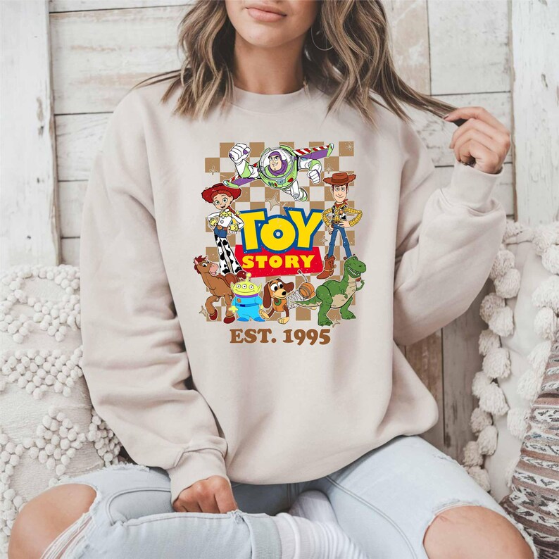 A woman wearing a beige sweatshirt with a graphic of characters from the Toy Story movie.