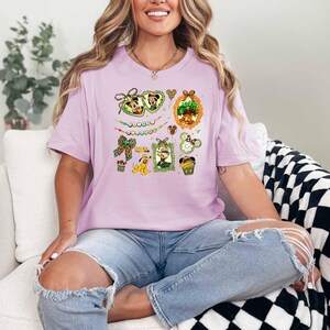 A woman wearing a pink t-shirt with a Disney-themed graphic is sitting on a white couch, smiling.