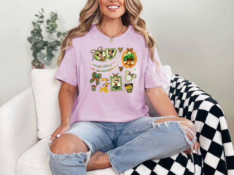 A woman wearing a pink t-shirt with a Disney-themed graphic is sitting on a white couch, smiling.