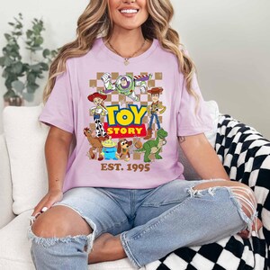 A woman wearing a pink t-shirt with a cartoon character design and text, sitting on a couch.