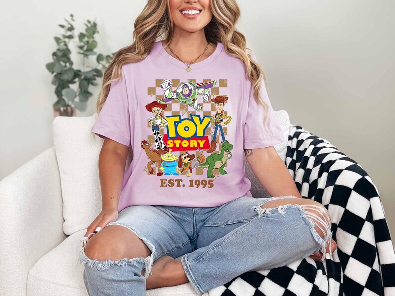 A woman wearing a pink t-shirt with a cartoon character design and text, sitting on a couch.