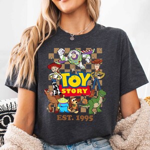 A woman wearing a gray t-shirt with a graphic of characters from the Toy Story movie, including Buzz Lightyear, Woody, and other beloved characters.