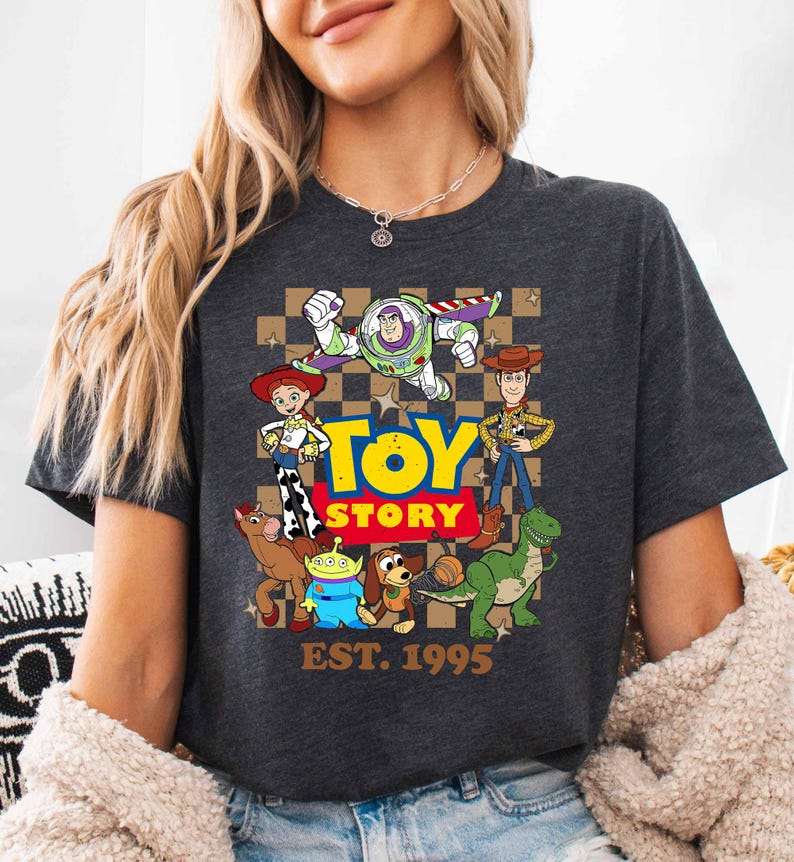 A woman wearing a gray t-shirt with a graphic of characters from the Toy Story movie, including Buzz Lightyear, Woody, and other beloved characters.