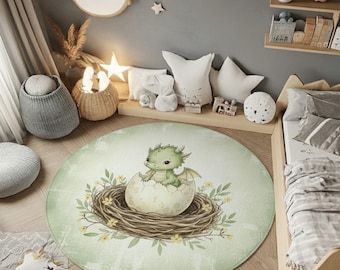 May include: A round rug featuring a baby green dragon hatching from an egg in a nest of twigs and leaves. The rug has a light green background with a watercolor effect, perfect for a nursery or children's room.
