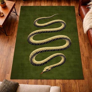 Puede incluir: Una alfombra rectangular verde con una ilustración detallada de una serpiente amarilla y negra que serpentea por la superficie. La cabeza de la serpiente es visible con una lengua roja. La alfombra está colocada sobre un suelo de madera.