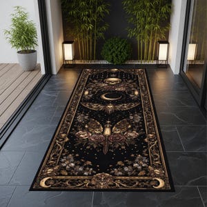 May include: Black rectangular rug with a detailed gothic design. The rug features a central moth and crescent moon motif, surrounded by roses, skulls, and ornate borders in gold and brown tones. The rug is placed on a dark tiled floor.