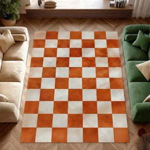 May include: A large, rectangular rug featuring a chequered design of orange and white squares. The rug is made of a soft material and is placed on a wooden floor. The rug is a decorative element for a living room, measuring approximately 200cm x 300cm.
