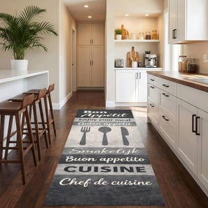 Könnte beinhalten: Ein rechteckiger Küchenteppich mit schwarz-grau-weißem Streifendesign. Der Teppich zeigt die Wörter "Bon Appétit", "Enjoy your meal", "Guten appetit", "Smakelijk", "Buon appetito", "CUISINE" und "Chef de cuisine". Der Teppich hat auch Utensiliensilhouetten.