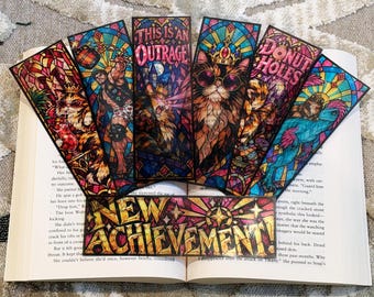 May include: A collection of six rectangular bookmarks featuring stained glass style illustrations. Designs include a cat with a crown, a muscular figure, a cat with sunglasses, and a dinosaur. Text reads THIS IS AN OUTRAGE, DONUT HOLES, and NEW ACHIEVEMENT!