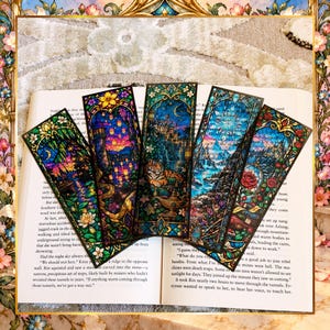 May include: Five rectangular bookmarks featuring colorful stained glass style illustrations. The designs depict various fantasy scenes including a tower with floating lanterns, a tiger with a golden lamp, a mountain landscape, and a red rose.