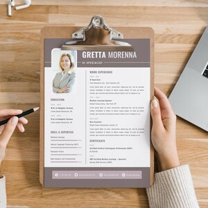 May include: A resume on a clipboard, featuring the name "Gretta Morenna" and the title "AI Specialist." The document details work experience, education, skills, and certifications. The resume is held by a person.