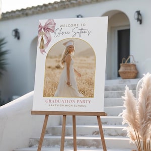 Puede incluir: Un letrero de bienvenida de graduación en un caballete de madera. El letrero presenta una foto de una graduada con birrete y toga, con el texto "Bienvenida a la fiesta de graduación de Olivia Sutton, Lakeview High School."