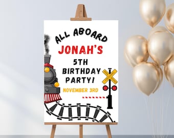 Puede incluir: Un letrero blanco sobre un caballete de madera con el texto "ALL ABOARD JONAH'S 5TH BIRTHDAY PARTY! NOVEMBER 3RD" y una ilustración de tren de dibujos animados. Globos dorados en el fondo.