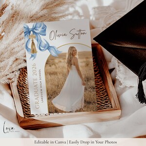 May include: A rectangular graduation announcement card featuring a light blue watercolor bow with a gold 2026 tassel charm. The text reads Olivia Sutton, Graduate 2026, and Lakeview High School. A central arch frames a photo of a person in a white dress.