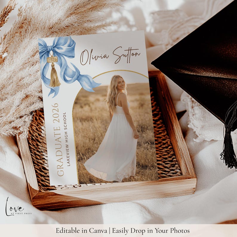 May include: A rectangular graduation announcement card featuring a light blue watercolor bow with a gold 2026 tassel charm. The text reads Olivia Sutton, Graduate 2026, and Lakeview High School. A central arch frames a photo of a person in a white dress.